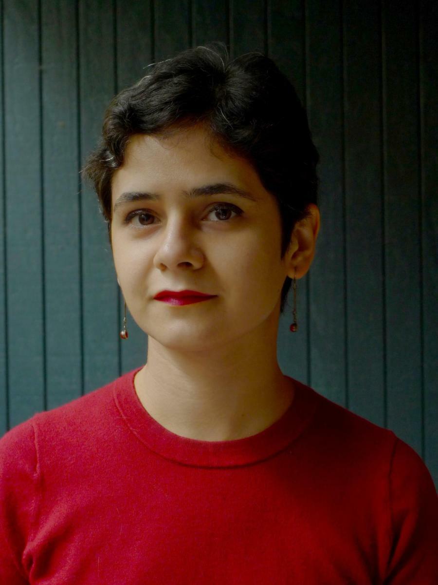 Wearing a bright red top and bright red lipstick, composer Aida Shirazi look directly into the camera