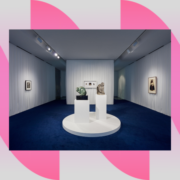 Image description: A room with ceiling to floor white curtains that cover all of the walls, and wall to wall navy blue carpet. There are two sculptures in the middle as well as three framed artworks on the walls.