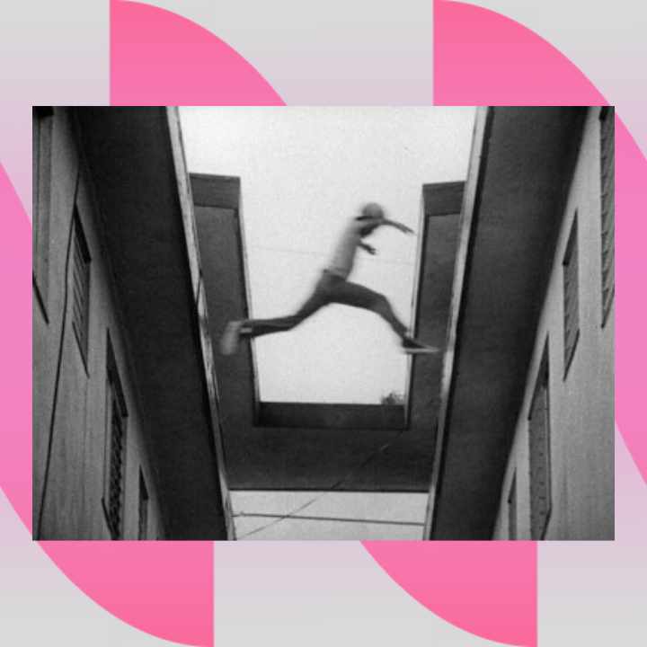 This is a still image from the film "Killer of Sheep" (1978) and depicts a young black boy jumping from one rooftop to another. It captures him in the gap between buildings.