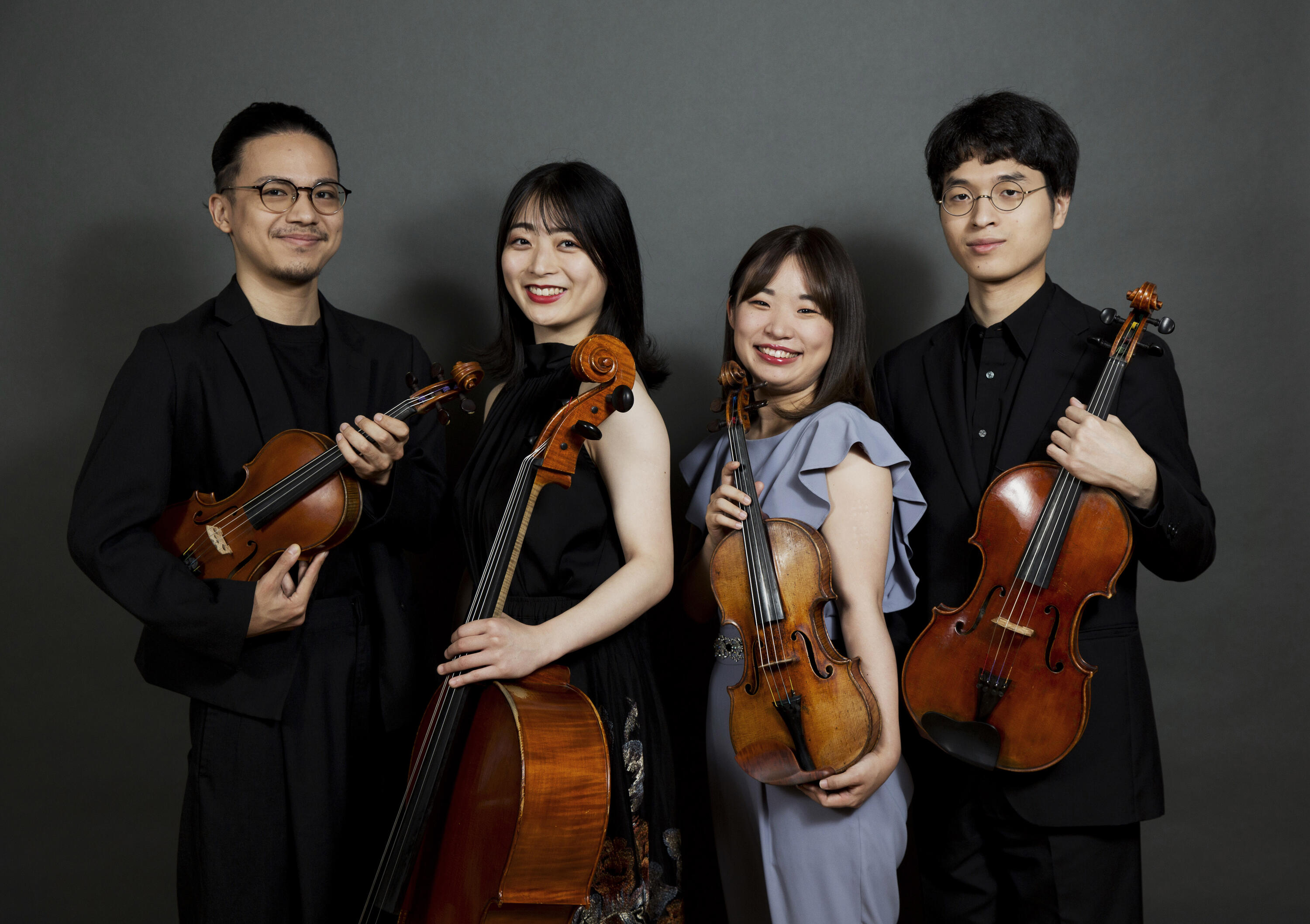 Members the Quartet Integra stand smiling and holding instruments in front of a gray background