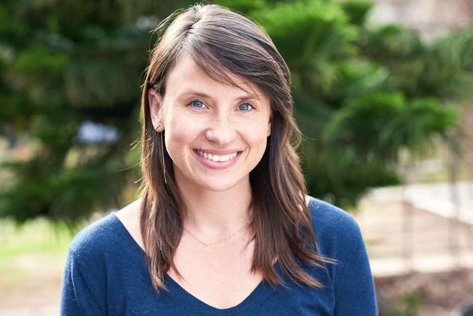 Emily is a white woman with medium length brown hair who’s smiling widely towards the camera.