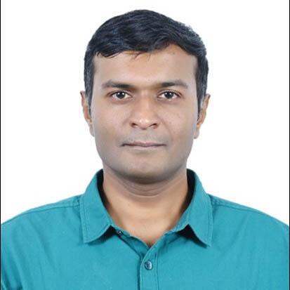 A man with dark skin and hair looks directly at the camera. He wears a teal open-collared button-down shirt