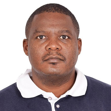 A black man with close cropped hair wears a blue knit shirt with a white collar