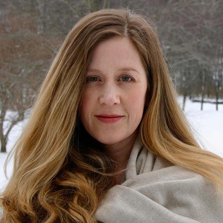 A middle-aged woman with long red-blond hair wears a beige wrap around her shoulders. The snowy ground is visible in the distance.