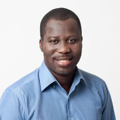A black man with close-cropped hair and a mustache wears an open collared blue shirt