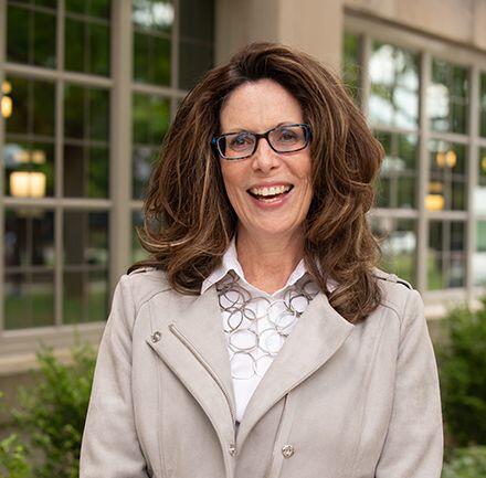 Smiling woman with shoulder length brown hair, with arms crossed