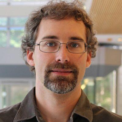 Man with curly brown hair, beard, and glasses