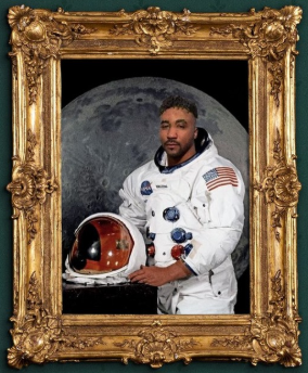 Eric is a man with short black hair and facial hair wearing a NASA space uniform.