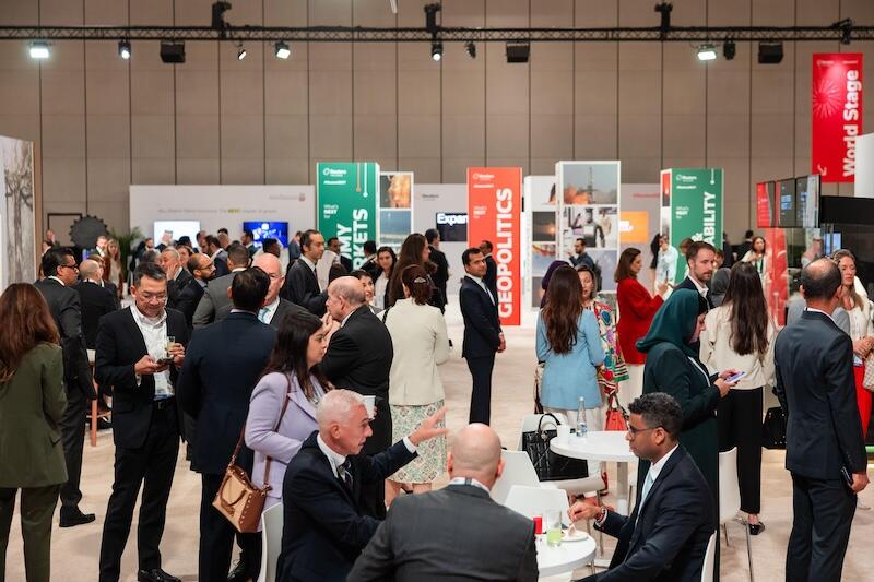 crowded reception/expo area with tall topic signs (e.g., "Politics," "Geopolitics," "World Stage").
