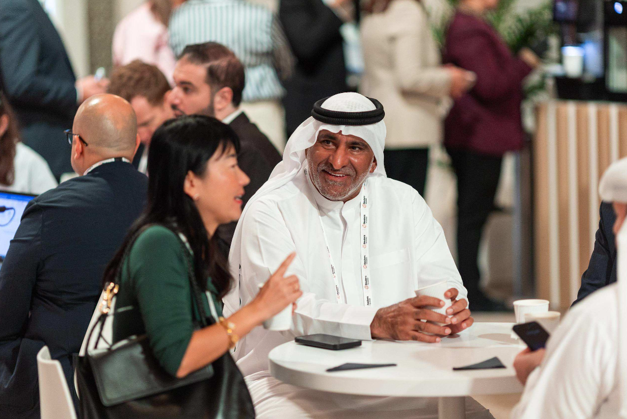 Attendees converse around a round table at the Reuters NEXT Gulf summit, including a man in traditional Emirati dress smiling as he speaks with a woman.