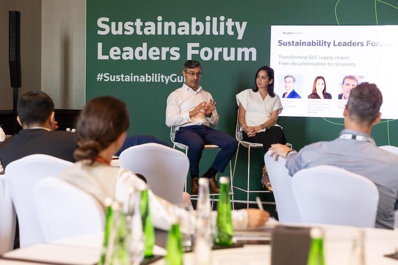 small talk with 2 speakers in front of a "Sustainability Leaders Forum" screen; audience seated at tables.