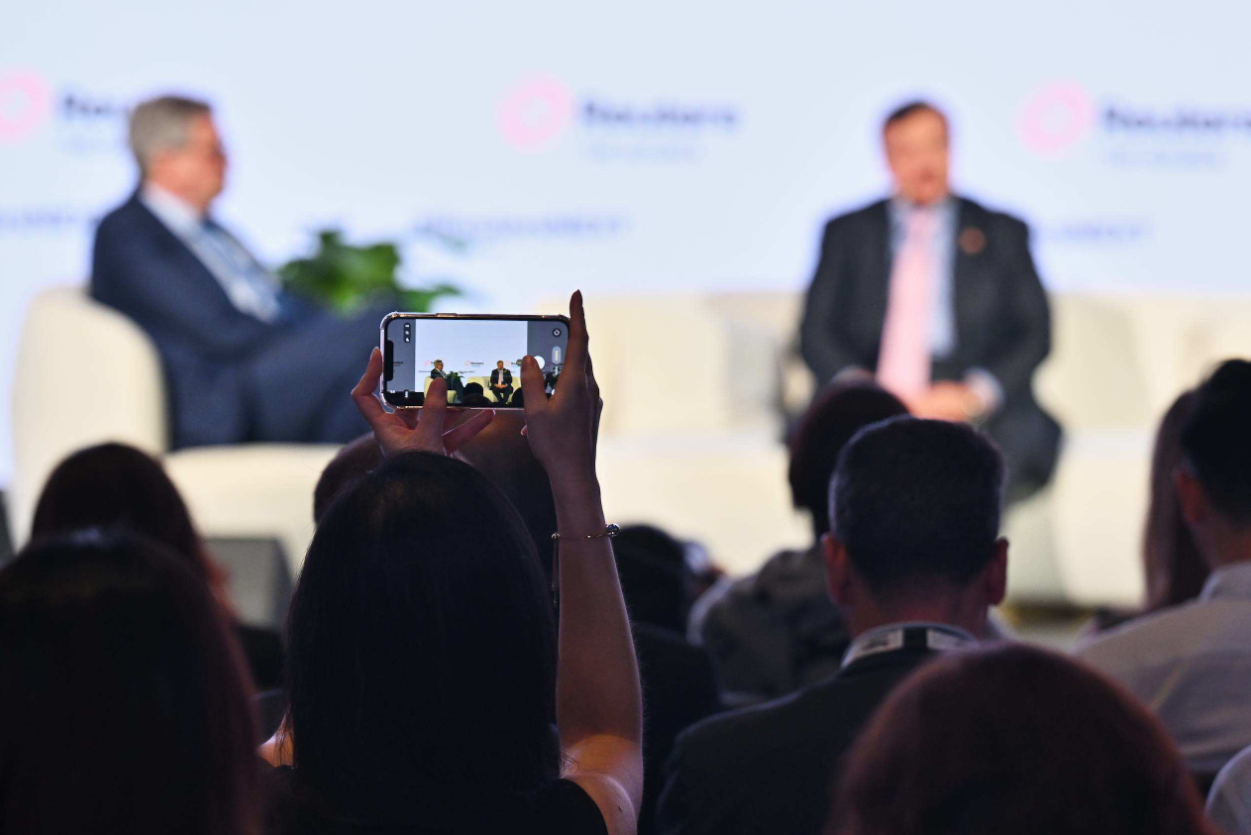 Audience member holds up a smartphone to photograph two speakers onstage during a Reuters NEXT Gulf summit panel discussion.