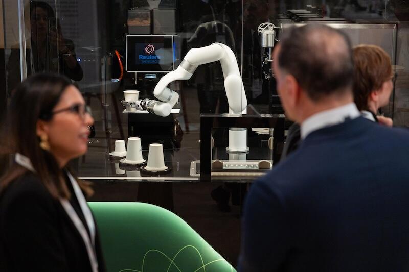 attendees talking by a glass display with a white robotic arm and cups.