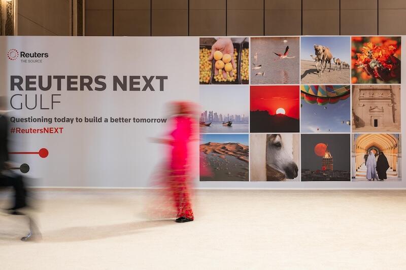"REUTERS NEXT GULF" step‑and‑repeat/photo wall with a grid of images.