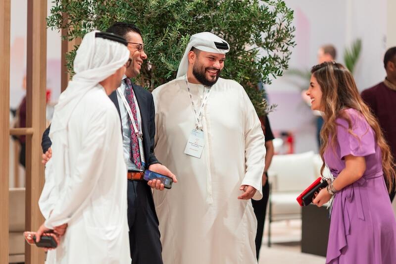 two men in white robes/headscarves talking with a woman in a purple dress.