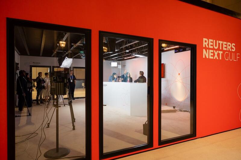 red "REUTERS NEXT GULF" wall with windows into recording/panel rooms.