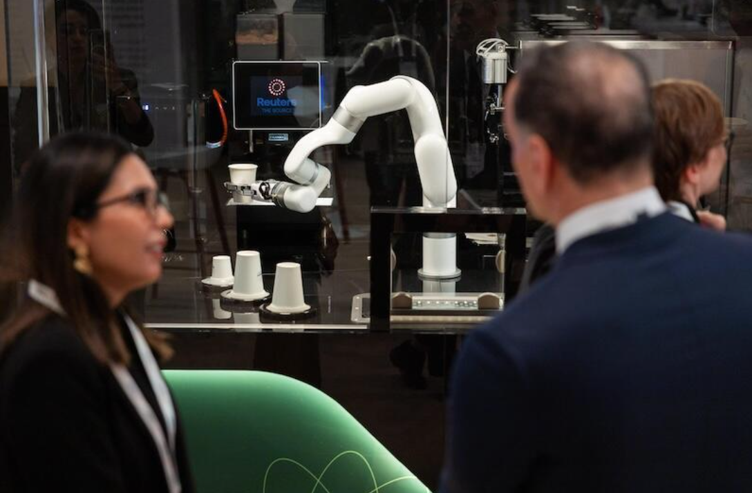 attendees talking by a glass display with a white robotic arm and cups.