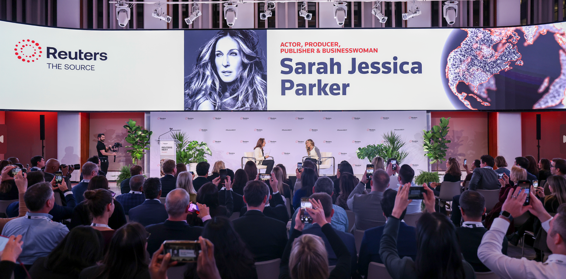 Wide view of the Reuters NEXT stage and audience, with a large screen introducing Sarah Jessica Parker and attendees raising phones to take photos.
