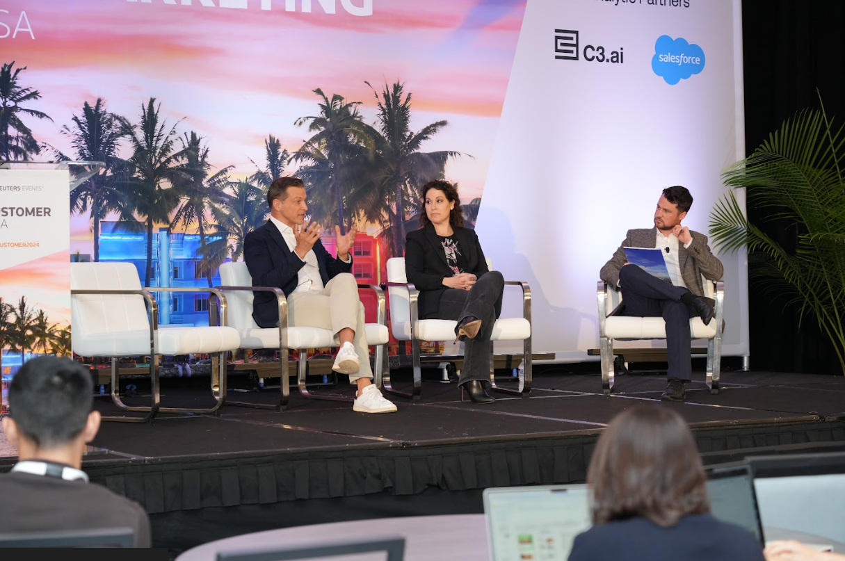 2 panelists and a moderator in dialogue on stage, taking questions and reacting to audience prompts