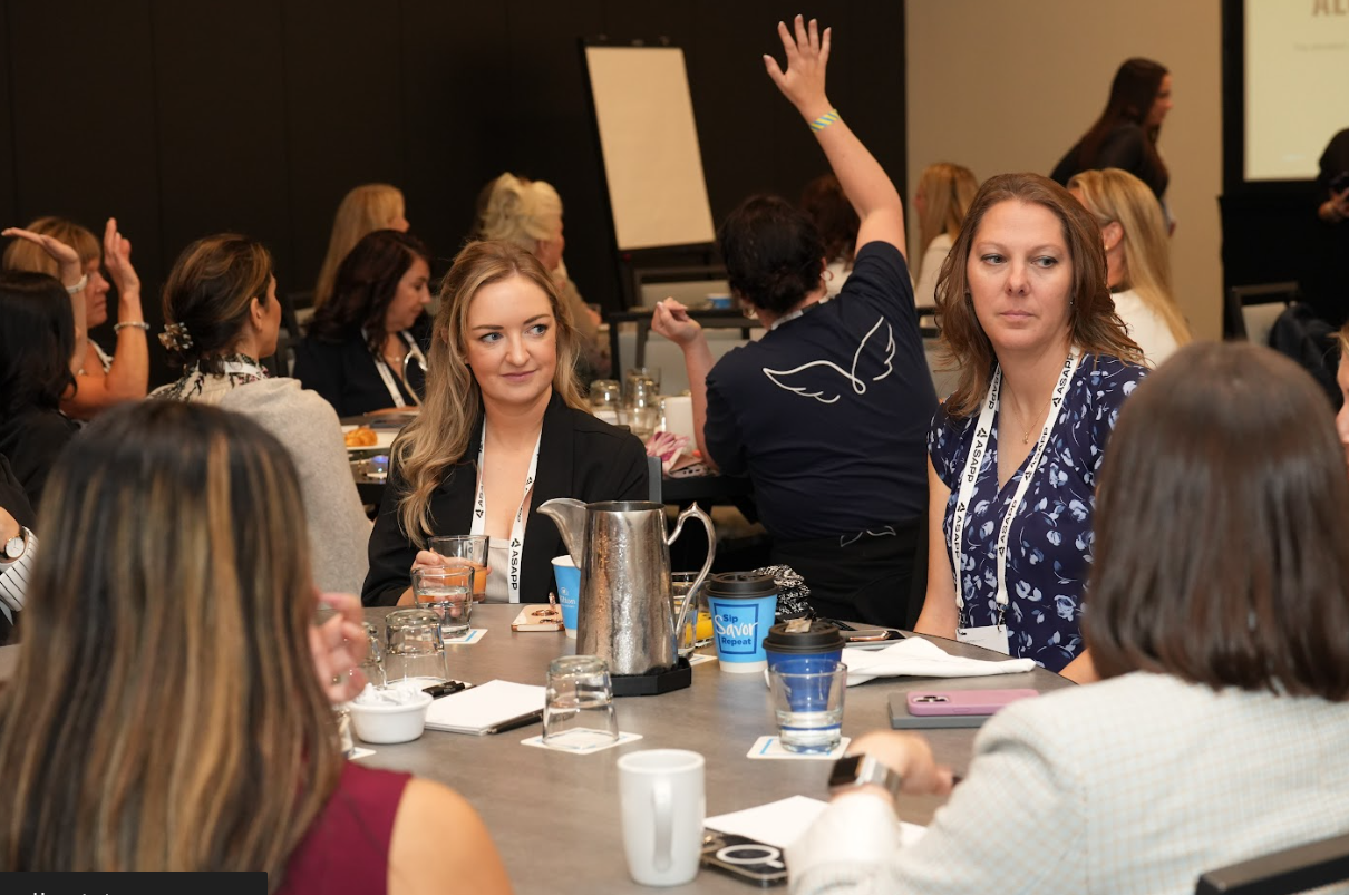 Participants at a roundtable discussion, one person raising a hand to contribute during an interactive marketing session.
