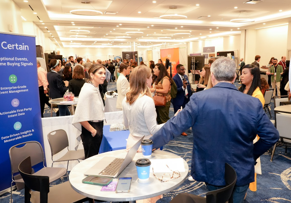 Busy expo hall with attendees networking and chatting around sponsor booths during an interactive break.