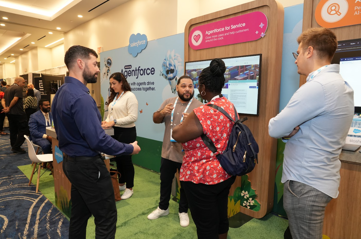 Exhibitor and attendees in animated discussion at a booth, pointing at screens during a product demo