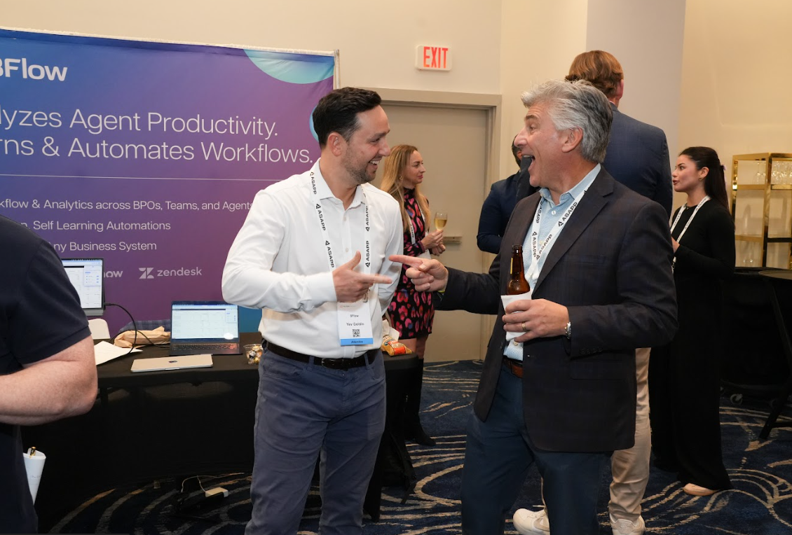 Two attendees enthusiastically exchanging ideas at a booth, gesturing as they compare notes