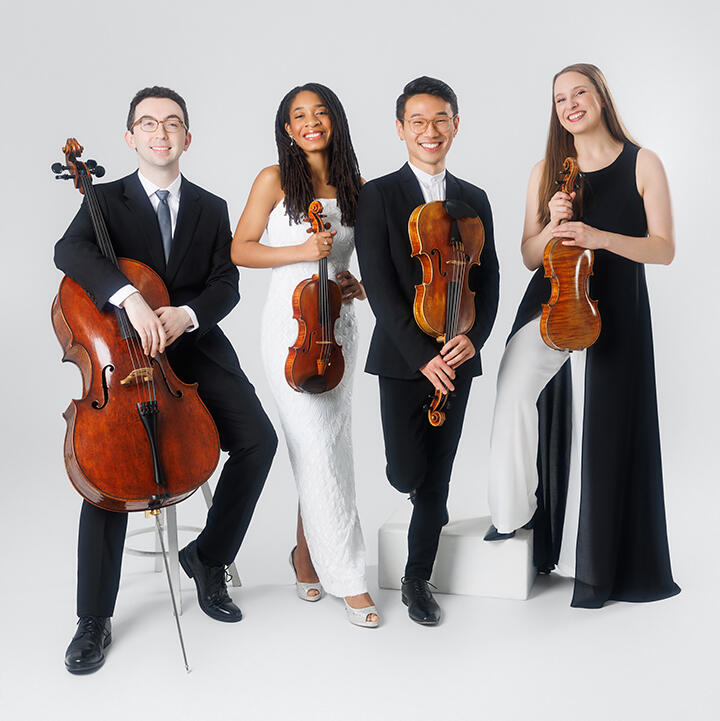Photo of the smiling members of the Abeo Quartet dressed formally, holding instruments. Left to right: white man, black woman, Asian man, white woman.