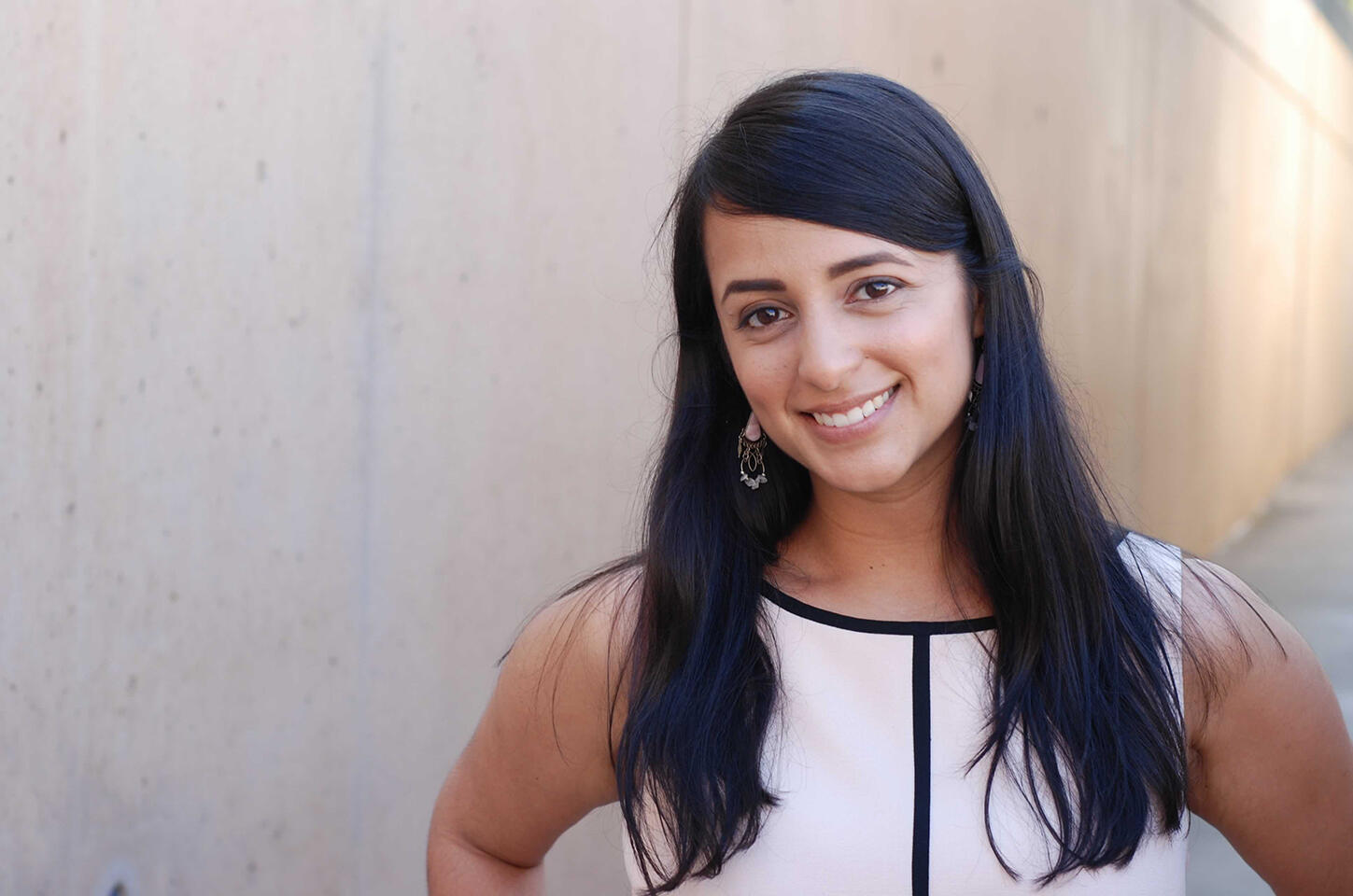 Color photo of Reena Esmail, a smiling young  woman with light brown skin and long black hair, wearing a sleeveless white top