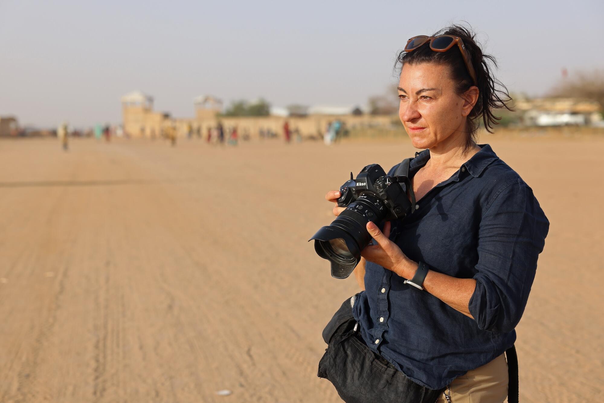Women standing in a sandy desert holding a professional camera.