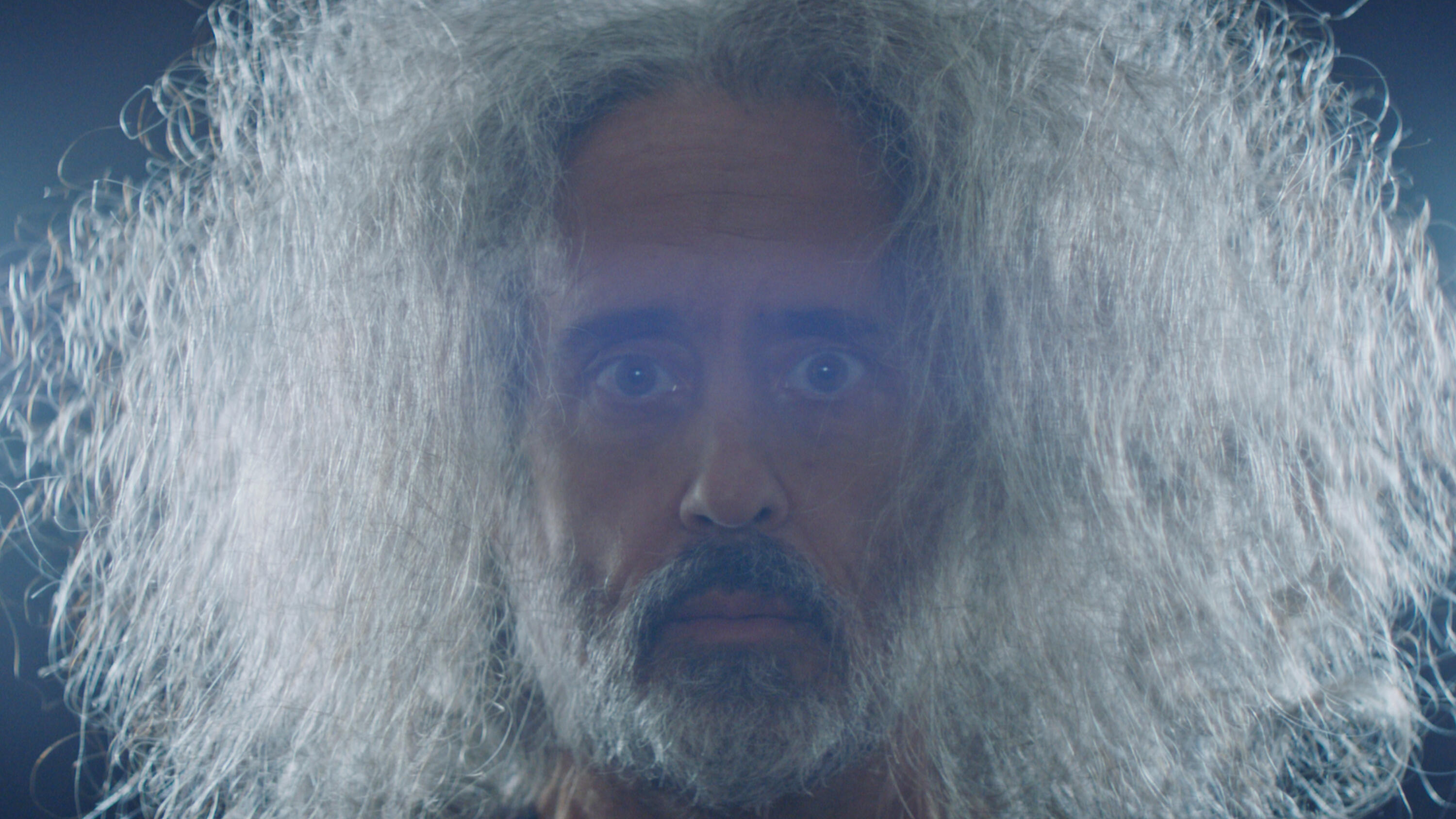Man staring into camera with long, gray, frizzy hair, beard, and moustache.