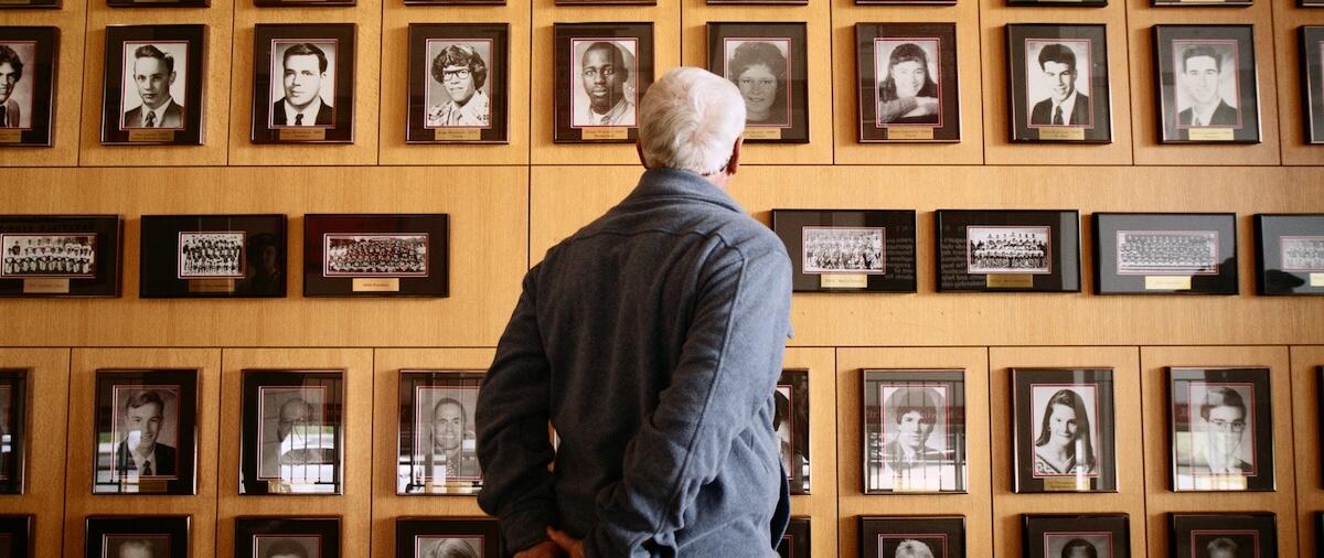 Older gentleman looking at a wall of plaques and photographs. 
