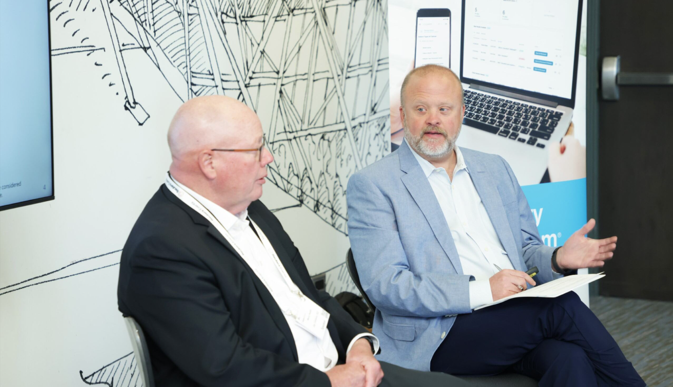 Two male speakers seated and in discussion at the Total Health conference, with a technology sponsor banner visible in the background.