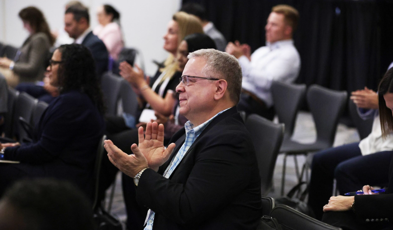 Speaker on stage at Reuters Events Total Health, seated with notes and lapel mic while discussing digital health and care delivery