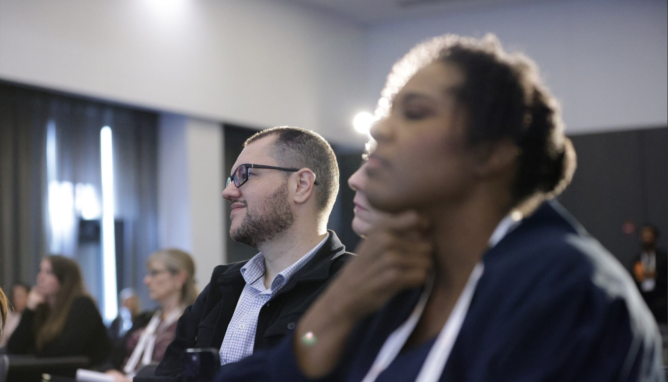 Two conference attendees listening attentively to a session at the Total Health conference, with other delegates visible in the background.