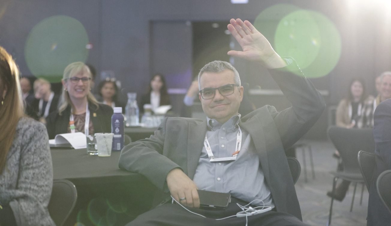 A conference attendee raising his hand to ask a question during a session at the Total Health conference, with other engaged attendees visible in the background.