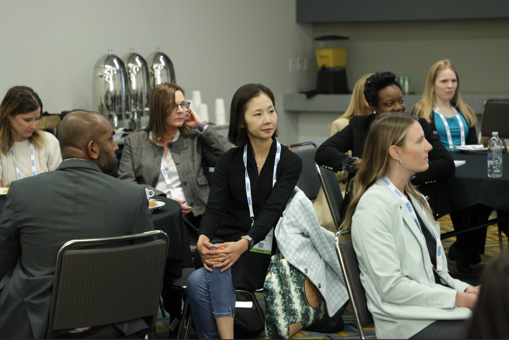 Breakout session at Reuters Events: Automotive USA, professionals seated at round tables with event badges, coffee service, and notebooks visible as they listen to the discussion.