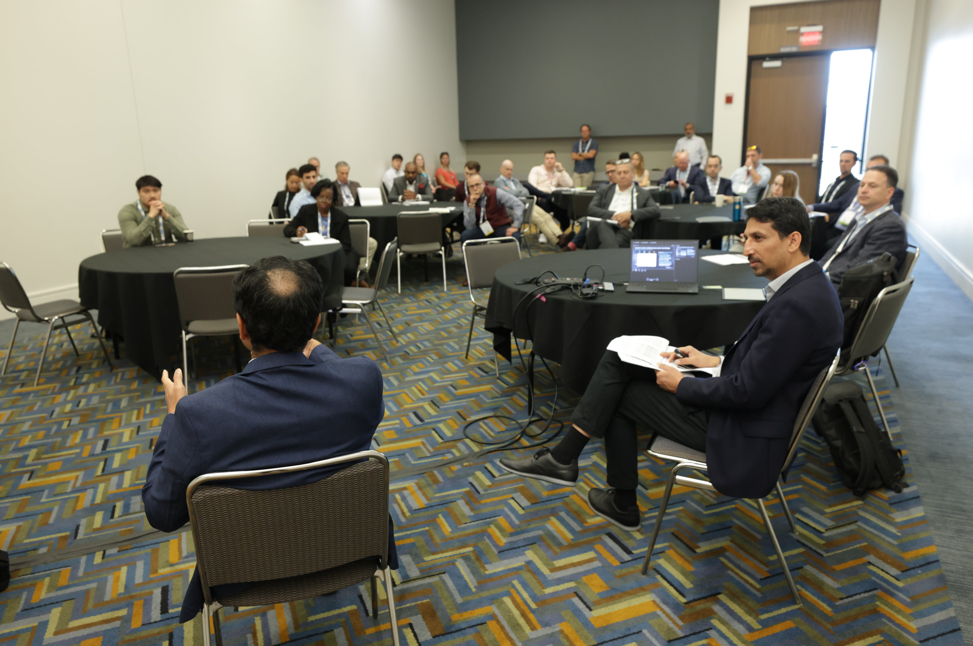 Breakout workshop at Reuters Events: Automotive USA, with a moderator and industry professionals engaged in discussion around round tables, laptop and presentation materials on the front table.