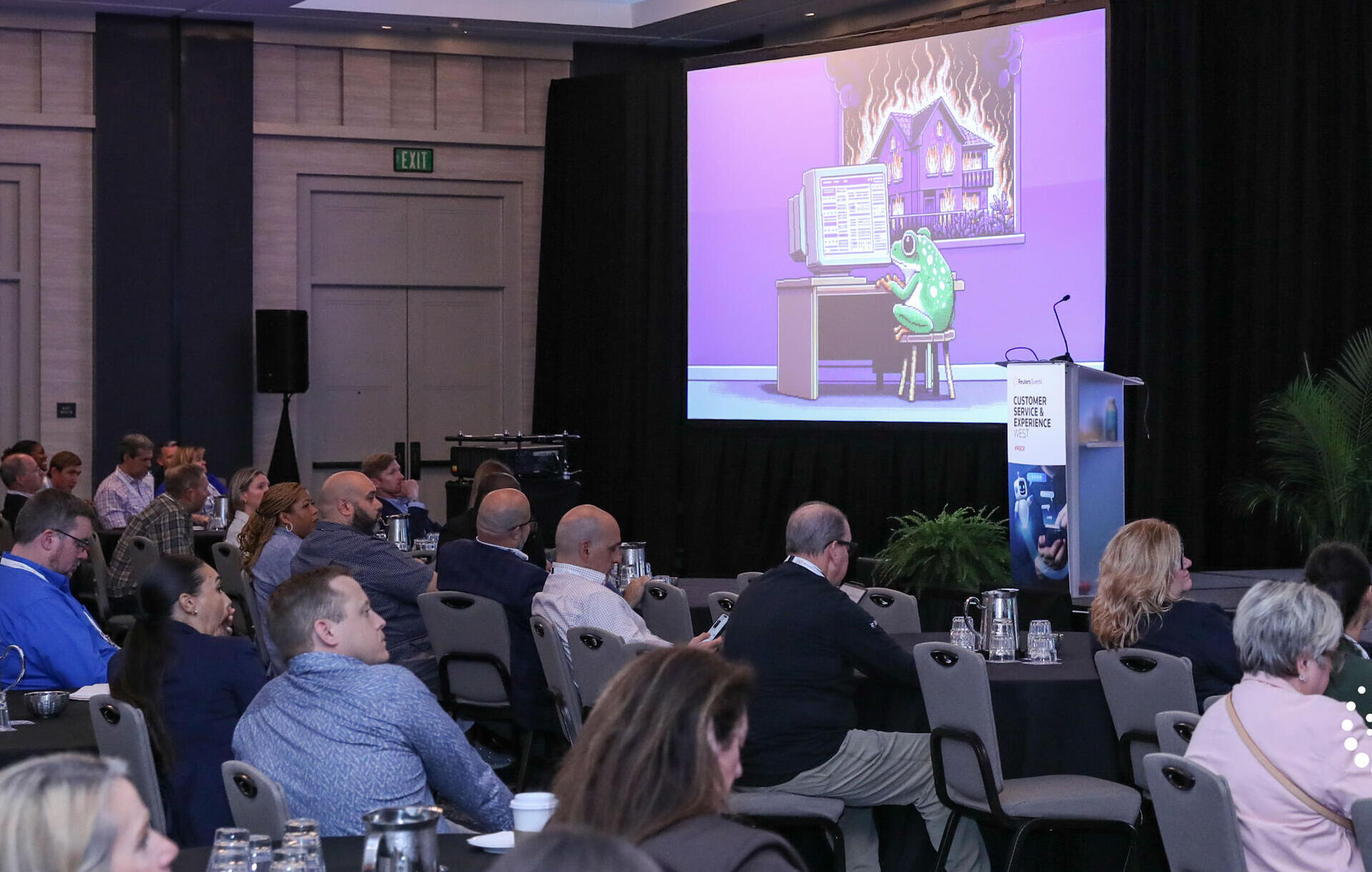 Customer Service & Experience conference keynote: audience watches humorous slide of a frog at a computer with a house on fire on screen