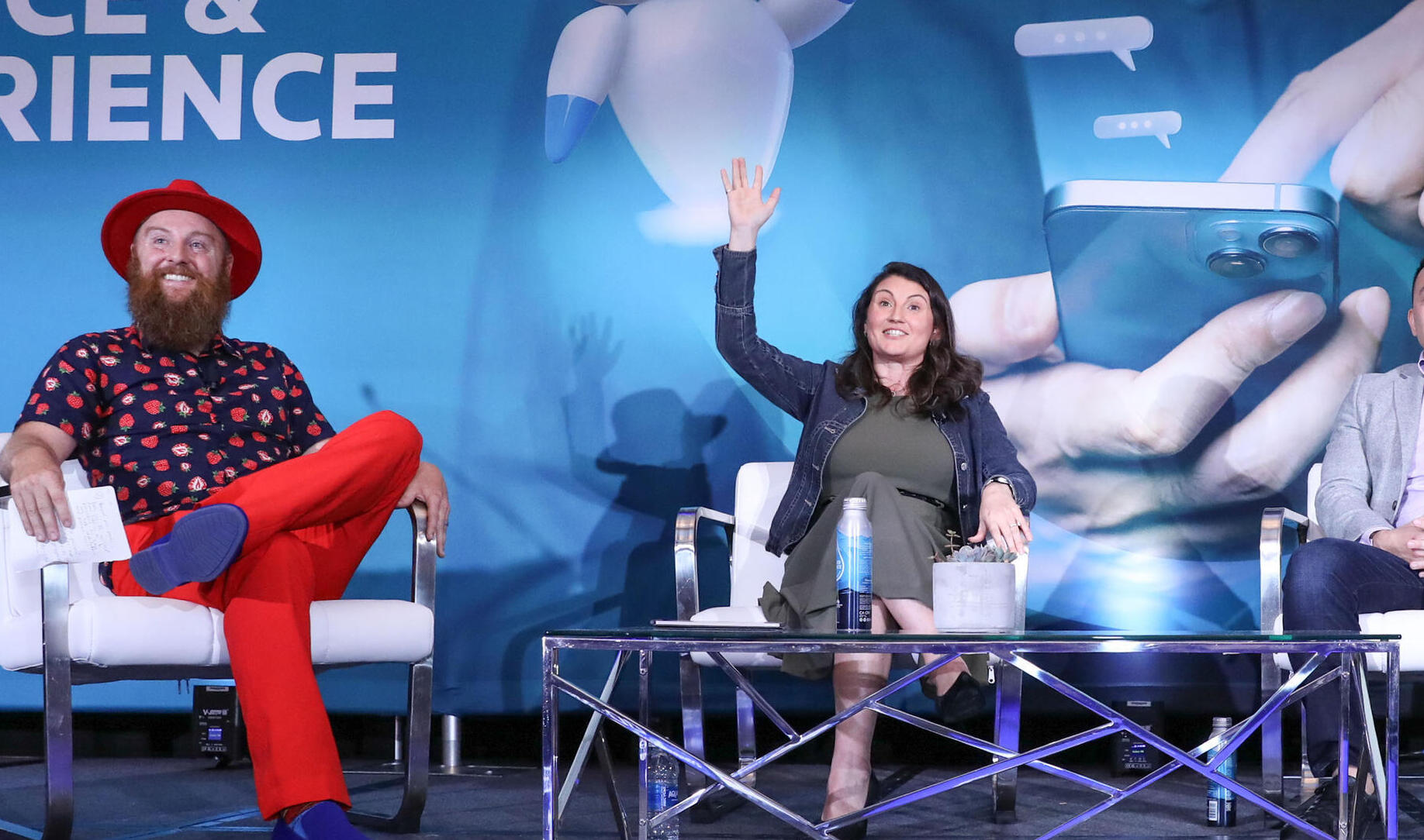 Customer Service & Experience conference panel: two speakers seated on stage, woman raises hand to engage audience during discussion