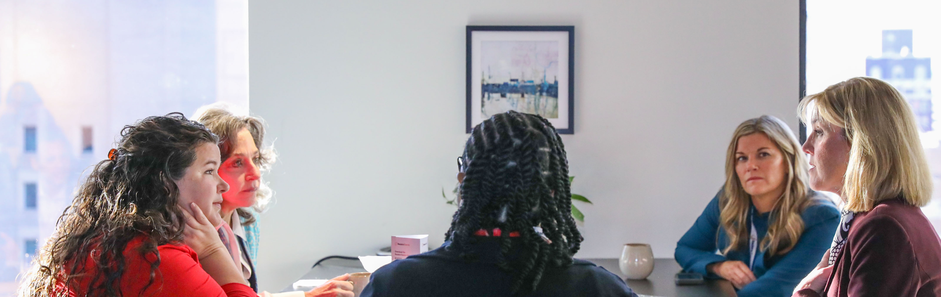 Five professionals seated around a dark conference table in a bright meeting room, engaged in discussion, with a framed artwork on the wall behind them. Reuters Events logo visible.