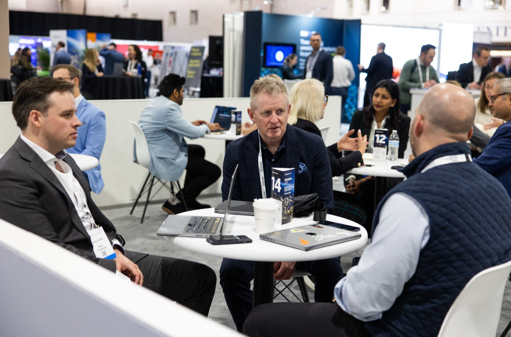 Attendees networking at roundtable meetings on the expo floor at a pharma industry conference.