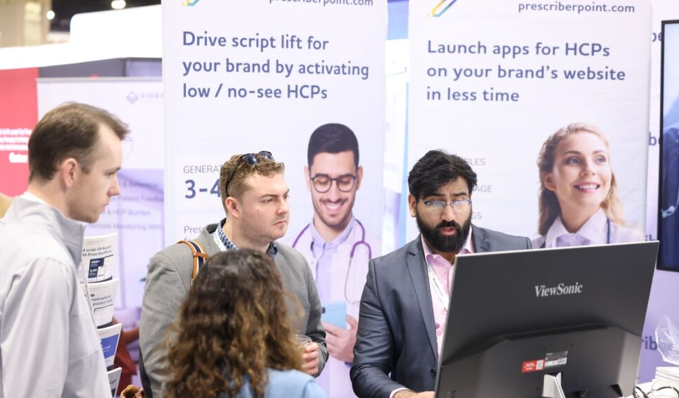 Exhibitor demos software at a monitor while attendees look on; banners promise "Drive script lift… activate low/no-see HCPs" and "Launch apps for HCPs."