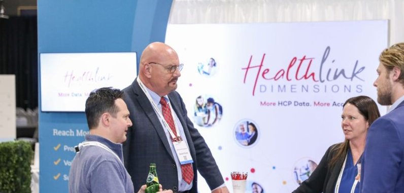 Small group talking at a Healthlink Dimensions booth; branded backdrop reads "More HCP Data. More Accurate."