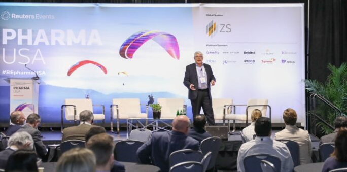 Presenter on PHARMA USA stage with sponsor logos including ZS; audience watches from round tables.