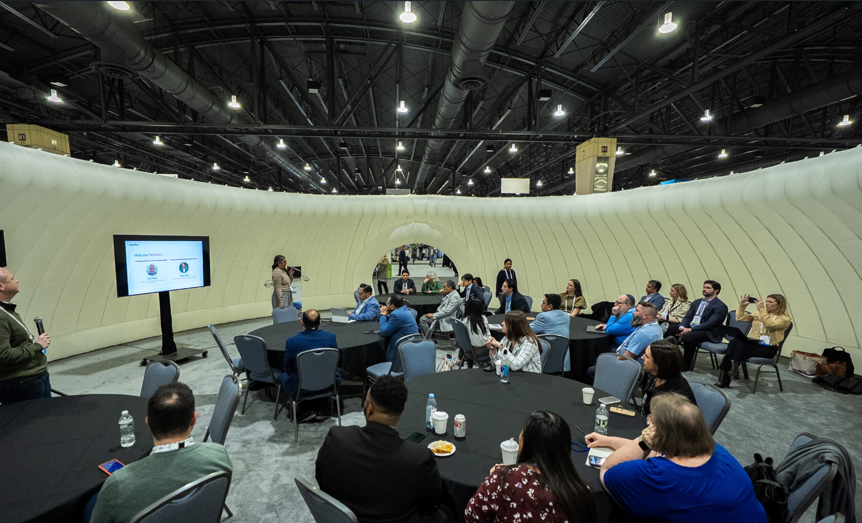 Presenter leading a roundtable session inside an inflatable dome structure at a trade show or conference.