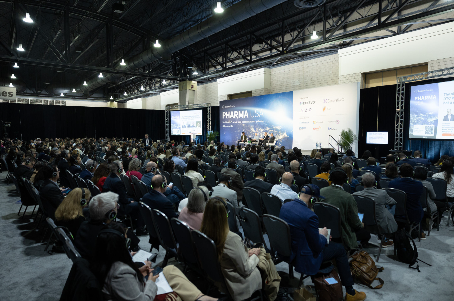 Panel discussion on stage at Pharma USA conference with a large seated audience wearing wireless headphones.
