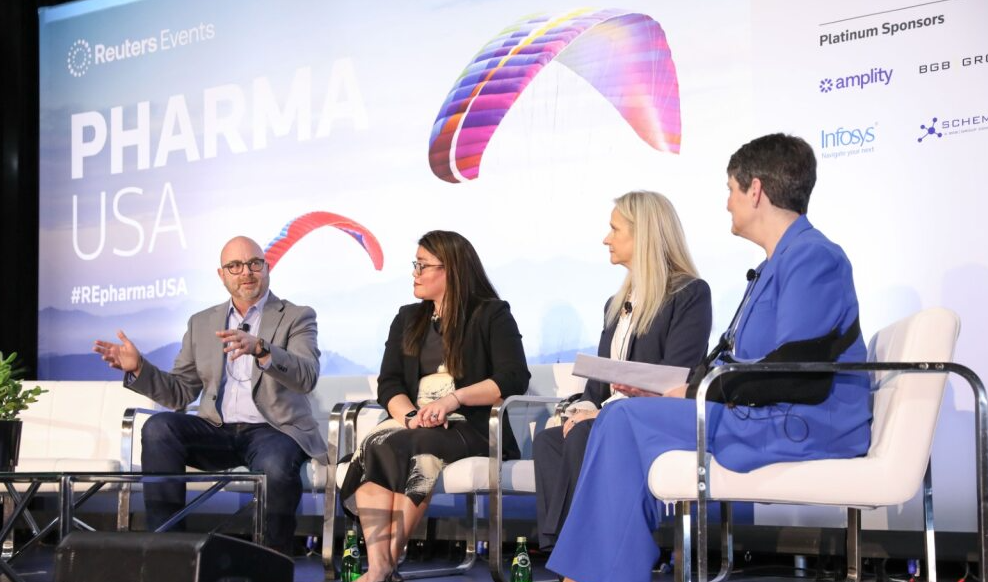Panel discussion on the PHARMA USA stage; four panelists seated with microphones, sponsor logos and paraglider artwork on backdrop.