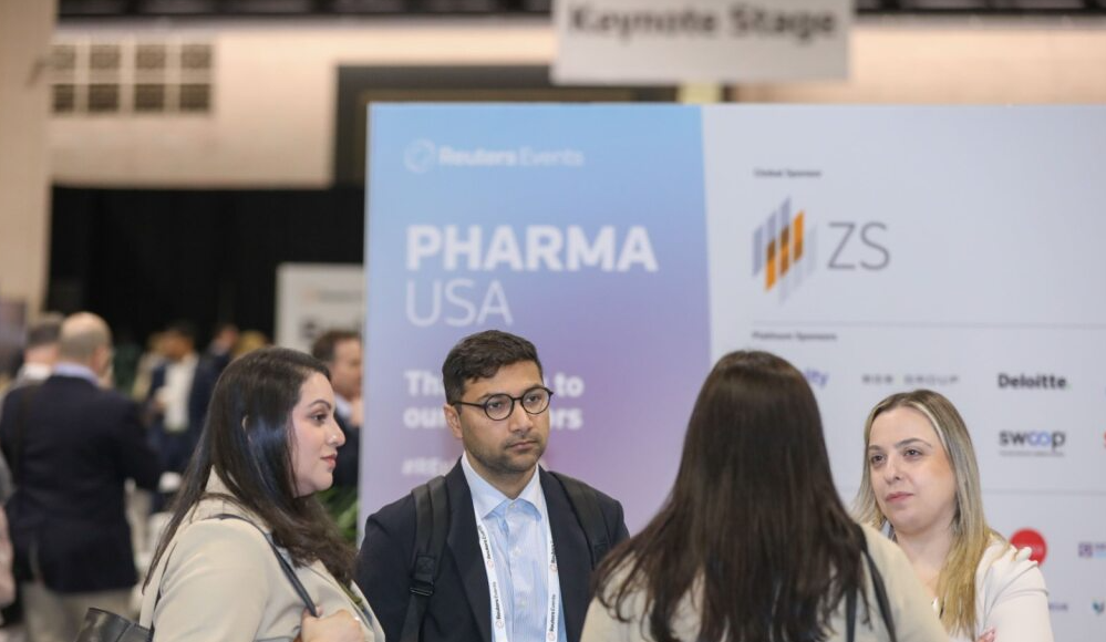 Group converses in front of a PHARMA USA sponsor board featuring ZS and other logos; "Keynote Stage" sign hangs above.