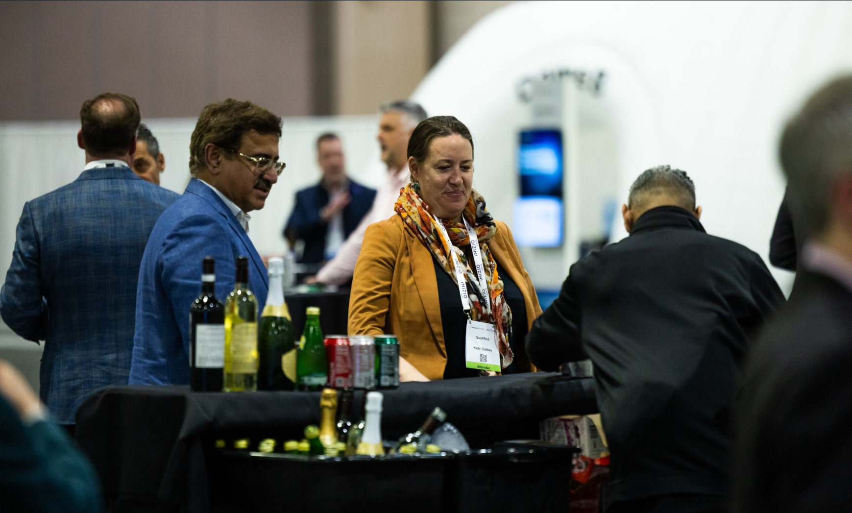Attendees networking around a drinks table at a pharma industry conference expo floor.